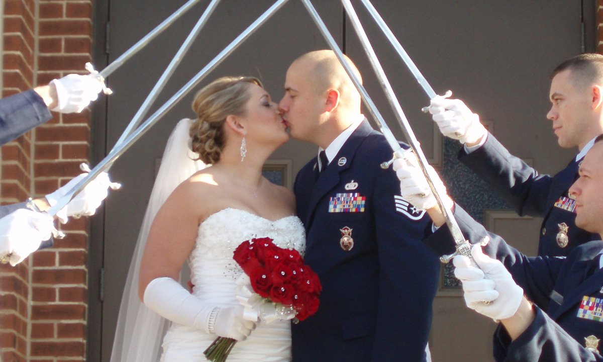 A bride and a groom in an Air Force dress uniform kiss under an arch of swords at a wedding venue and reception hall in Beaver Dam, WI.