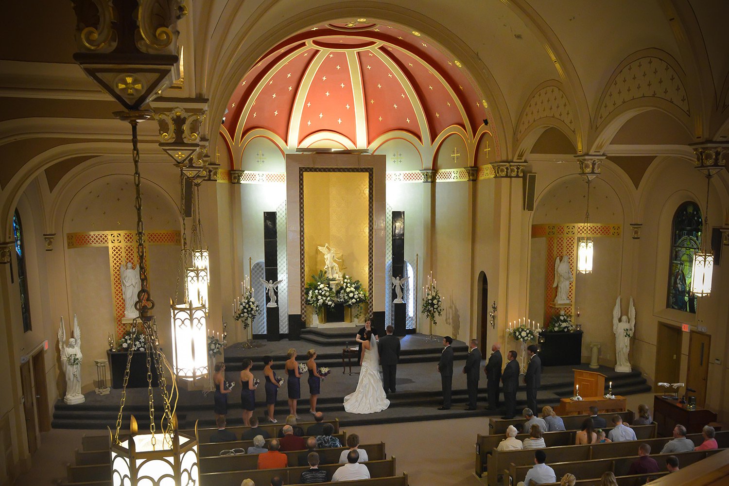 A bride and groom stand at the altar of a wedding venue in Beaver Dam, WI, during their ceremony, surrounded by their bridal party and guests in the pews.